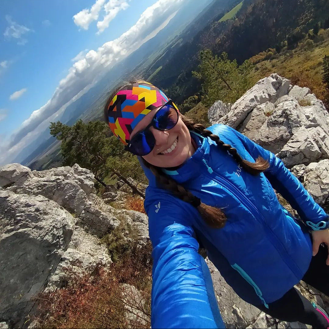 Person in blue jacket and colorful helmet on a rocky mountain top with a scenic view.