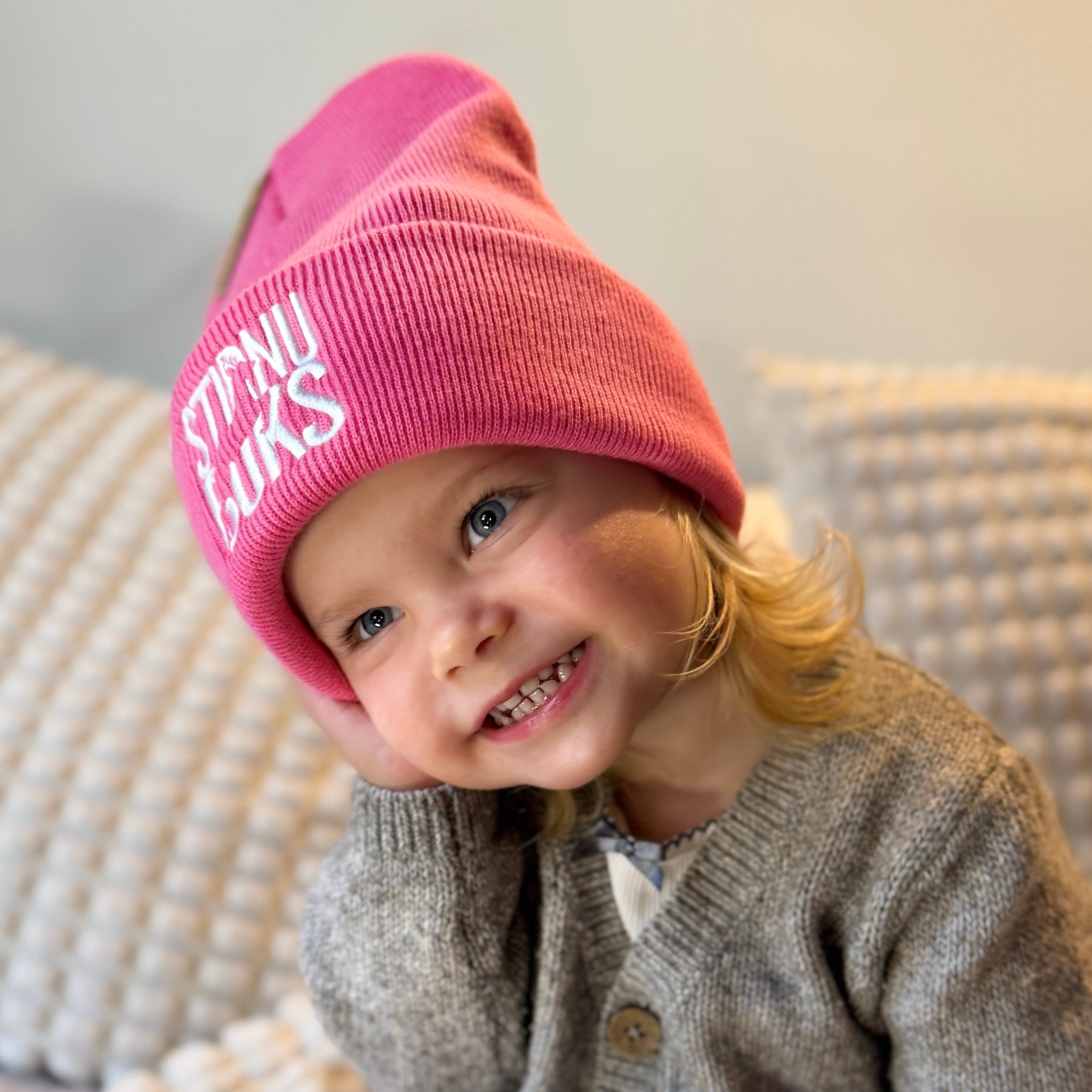 Child wearing a pink beanie with text, sitting on a textured surface.
