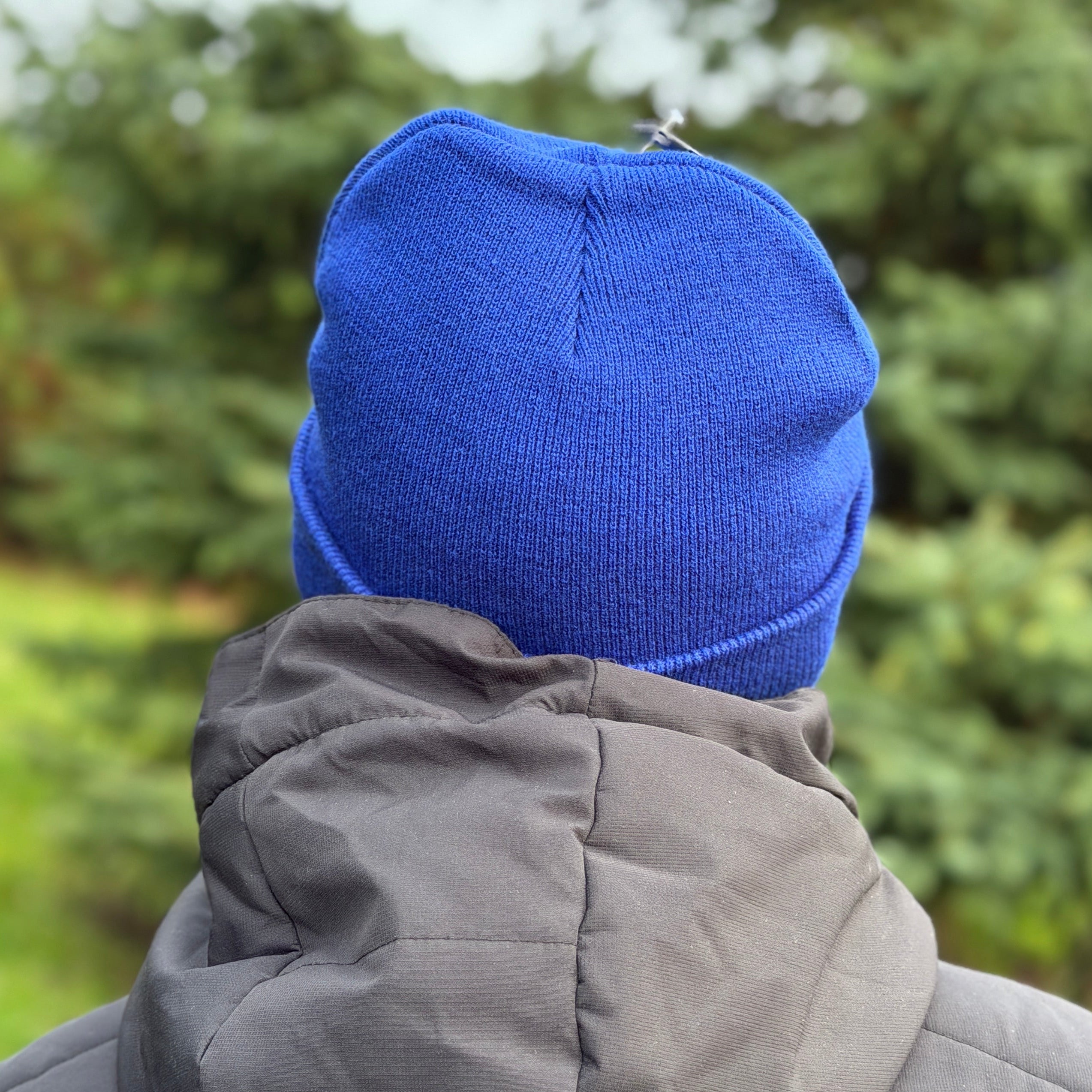 Person wearing a blue beanie and gray jacket in a forest setting