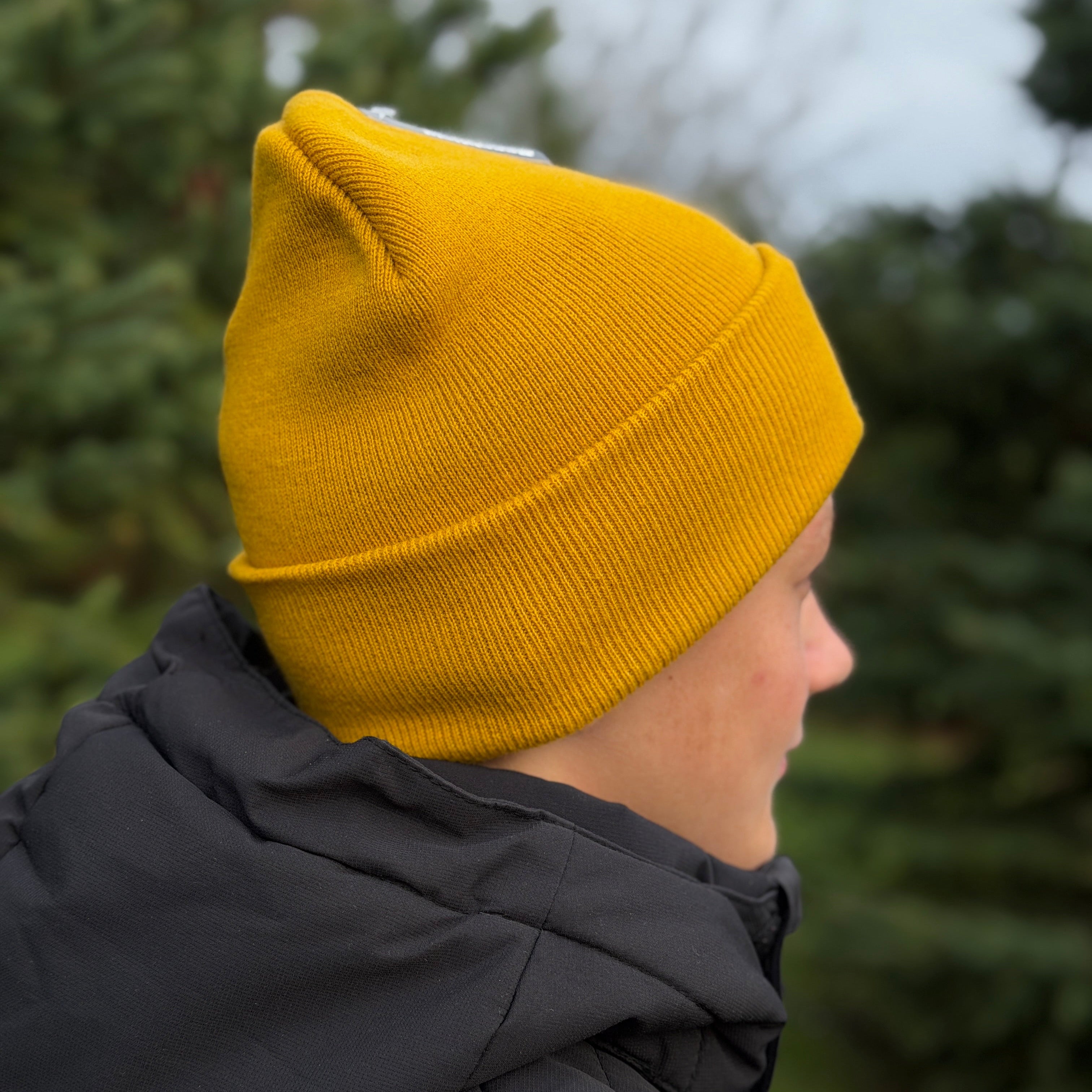 Person wearing a yellow beanie and dark coat with a blurred green background