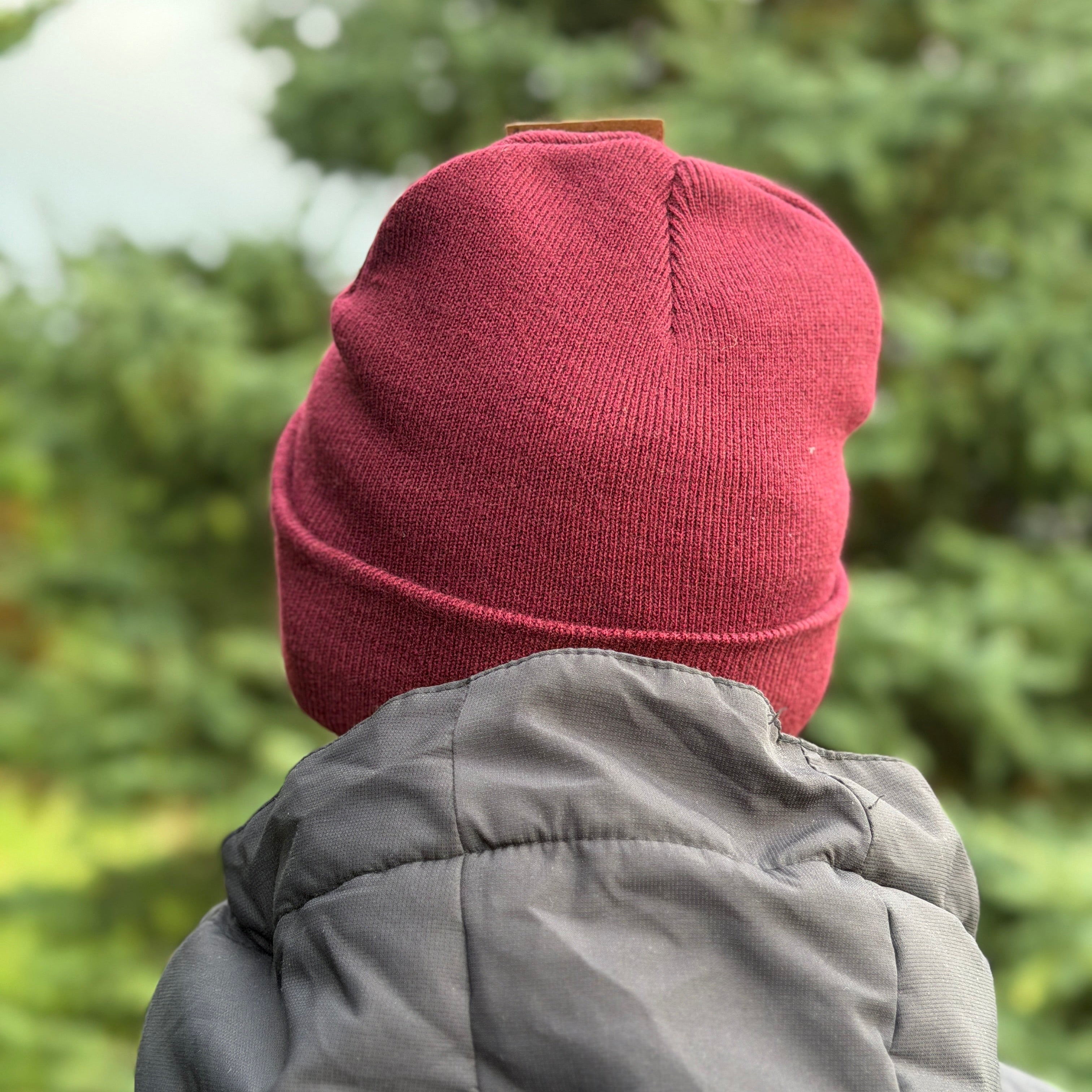 Person wearing a red beanie and gray coat with a blurred green forest background