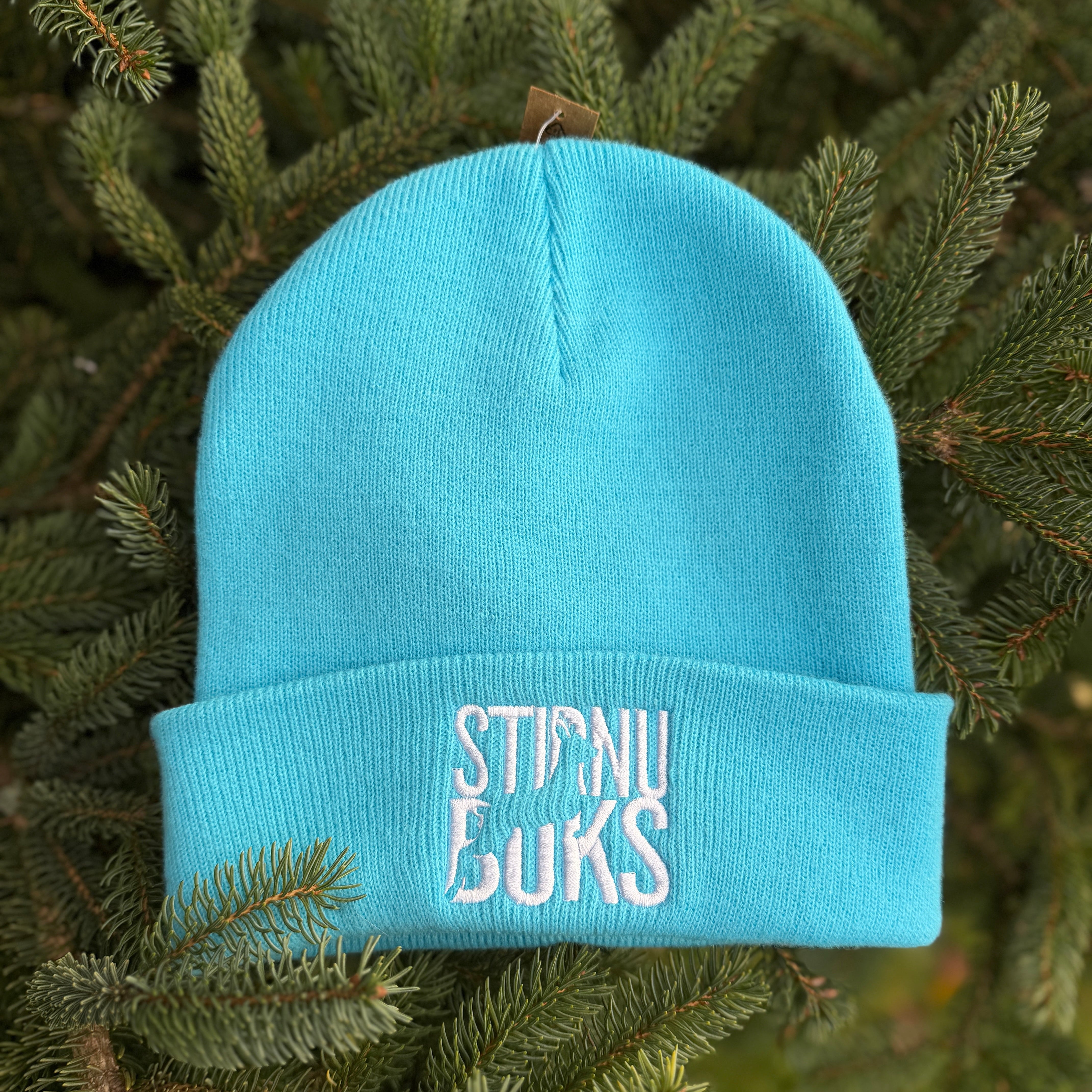 Blue beanie with 'STIRNU BUKS' embroidery on a green leafy background