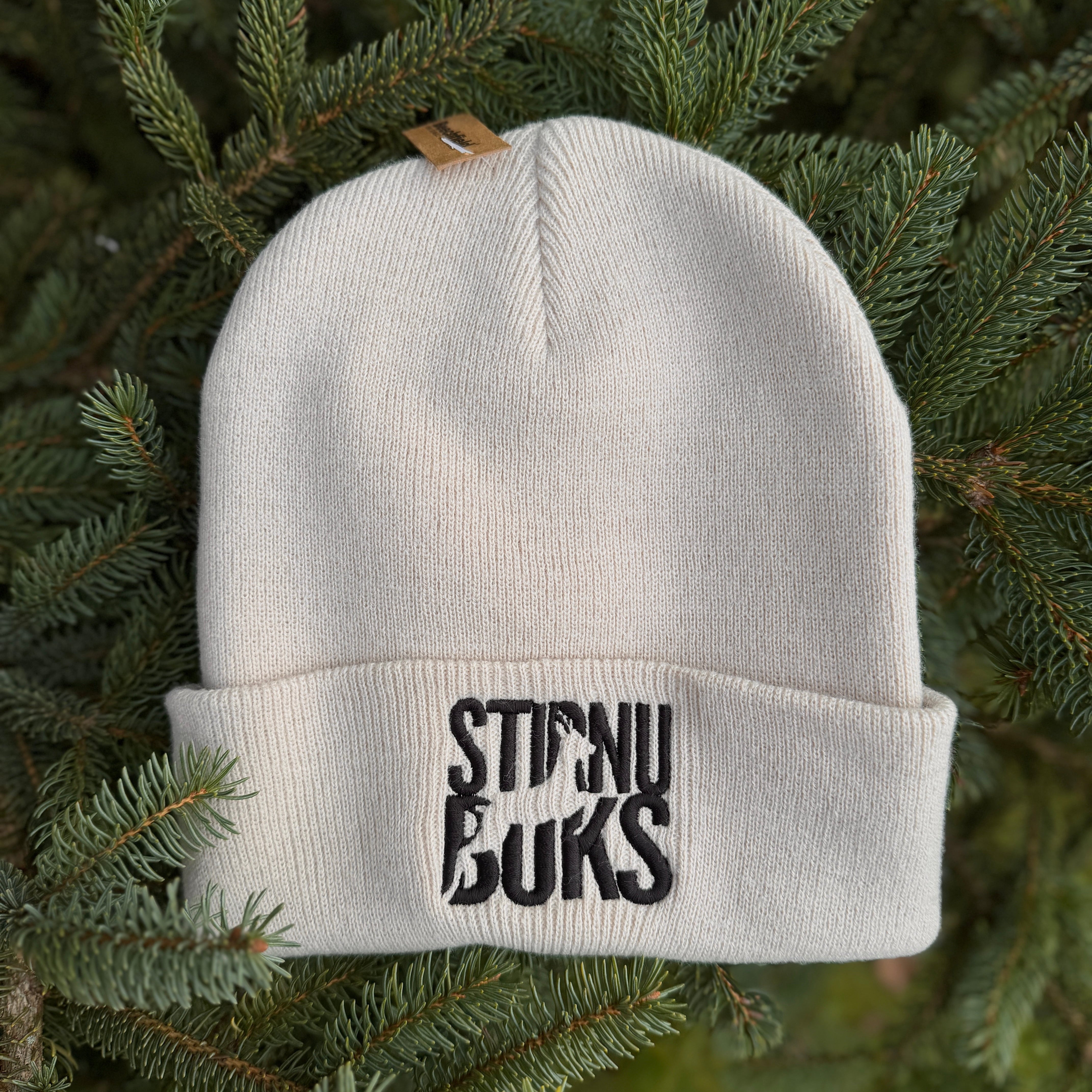 White beanie with 'STIRNU BUKS' text on a green leafy background