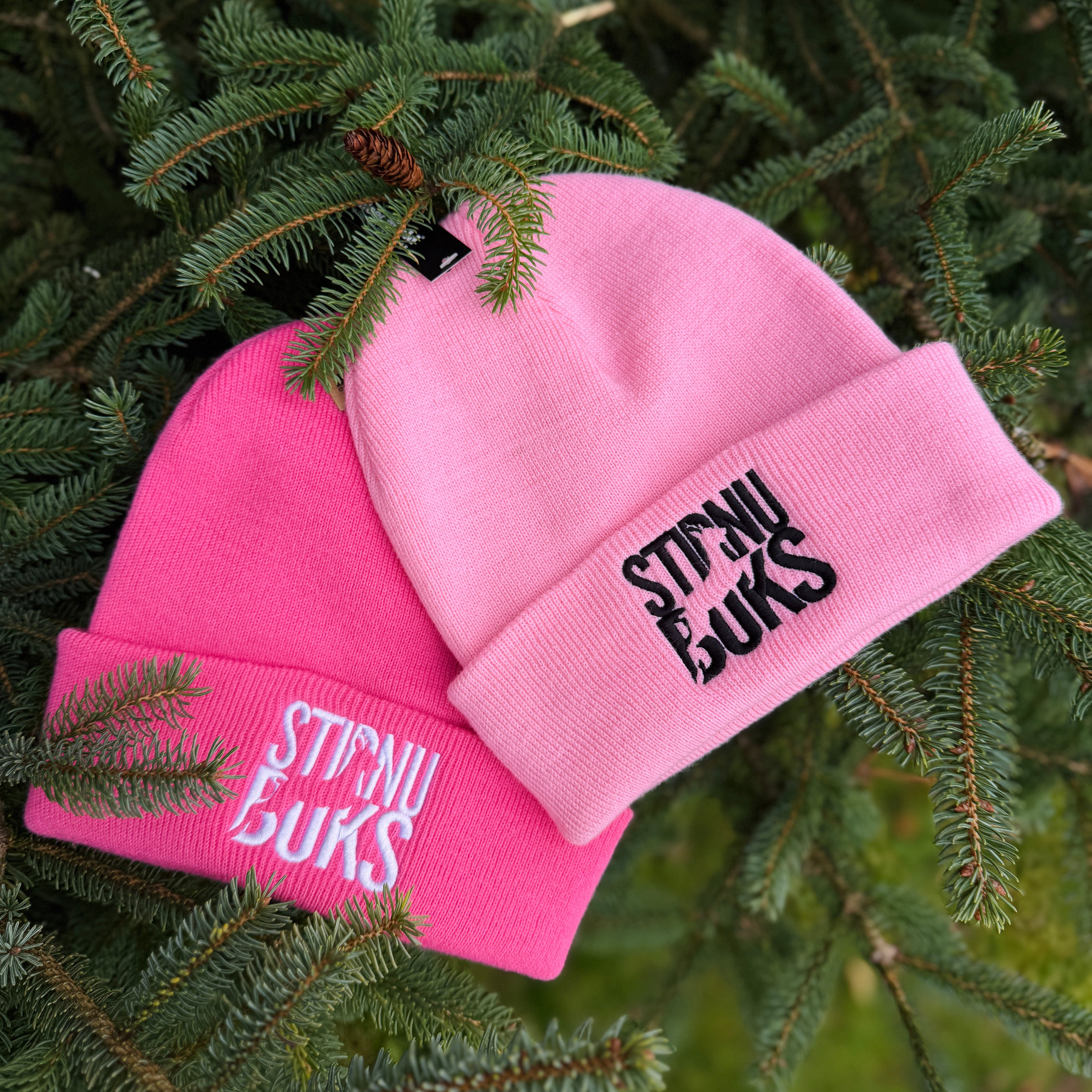 Pink beanie with 'STIRNU BUKS' text on a green leafy background