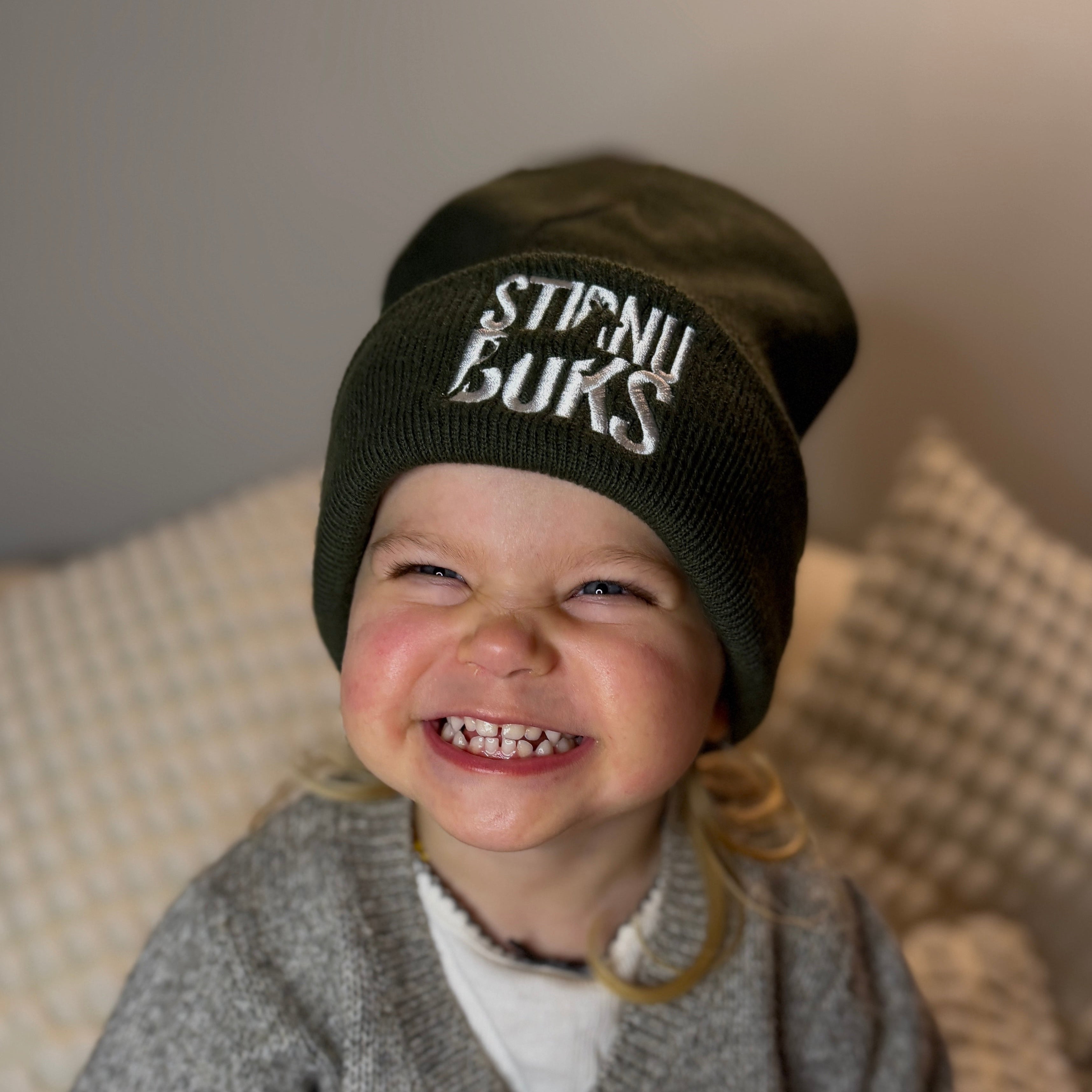 Child wearing a black beanie with 'Stirnu buns' logo, smiling on a neutral background