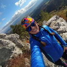 Person in blue jacket and colorful helmet on a rocky mountain top with a scenic view.