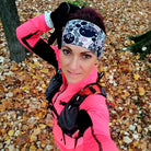 Person in bright pink athletic outfit with black accents standing on a leaf-covered ground.