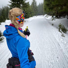 Person in a blue jacket skiing on a snowy trail with colorful goggles.