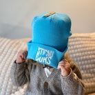 Child wearing a blue beanie with text, sitting on a textured surface.