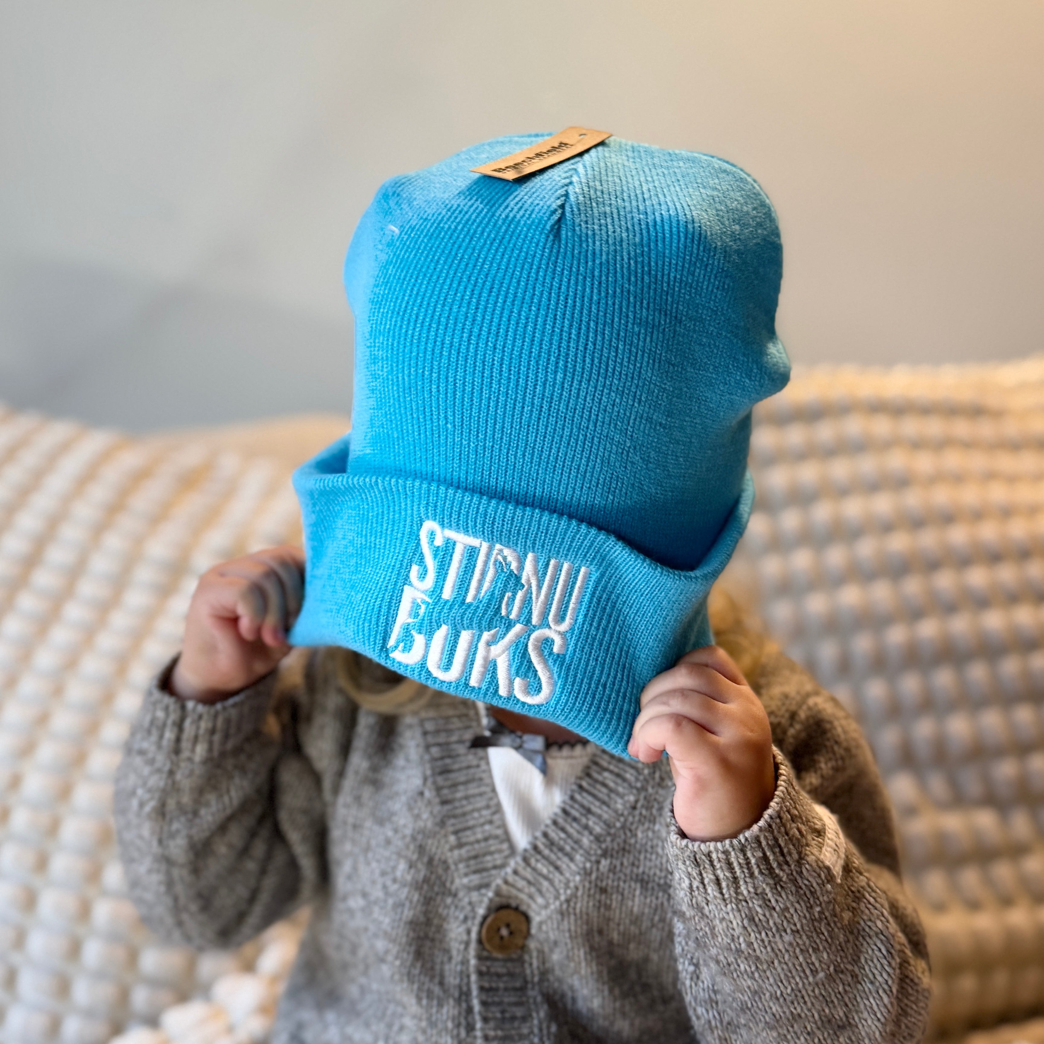 Child wearing a blue beanie with text, sitting on a textured surface.