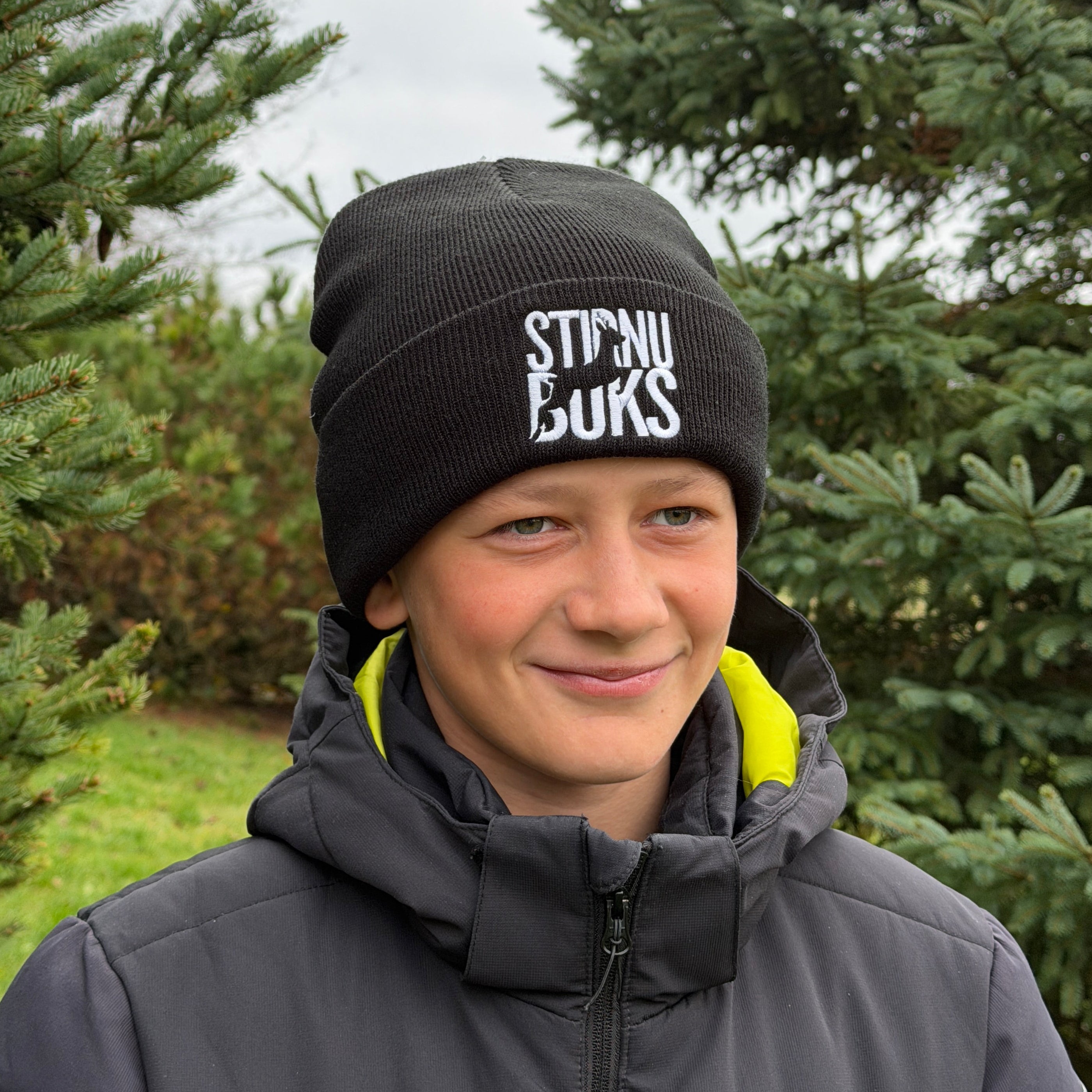 Person wearing a black beanie and gray jacket with trees in the background