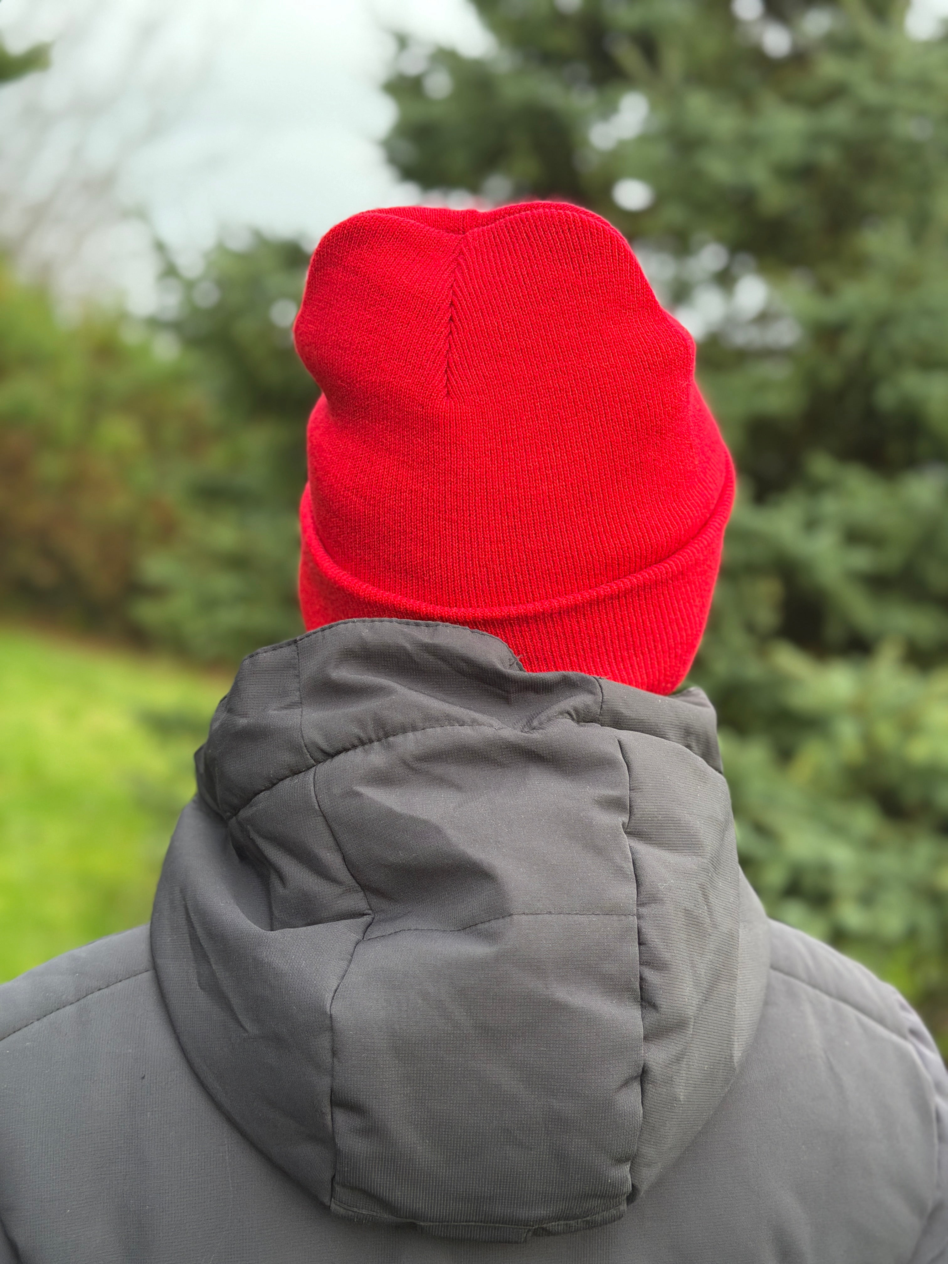 Person wearing a red beanie and gray coat with a blurred green outdoor background