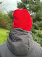 Person wearing a red beanie and gray coat with a blurred green outdoor background