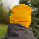 Person wearing a yellow beanie and dark jacket with a blurred natural background