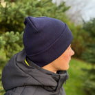 Person wearing a navy beanie and dark jacket outdoors with trees in the background