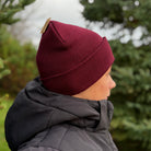 Person wearing a maroon beanie and dark jacket in a forest setting