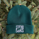 Green beanie with 'STIRNU BUKS' text on a green leafy background