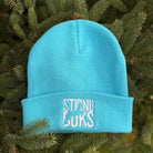 Blue beanie with 'STIRNU BUKS' embroidery on a green leafy background