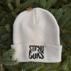 White beanie with 'STIRNU BUKS' text on a green leafy background