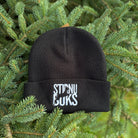 Black beanie with 'STIRNU BUKS' text on a green pine branch background