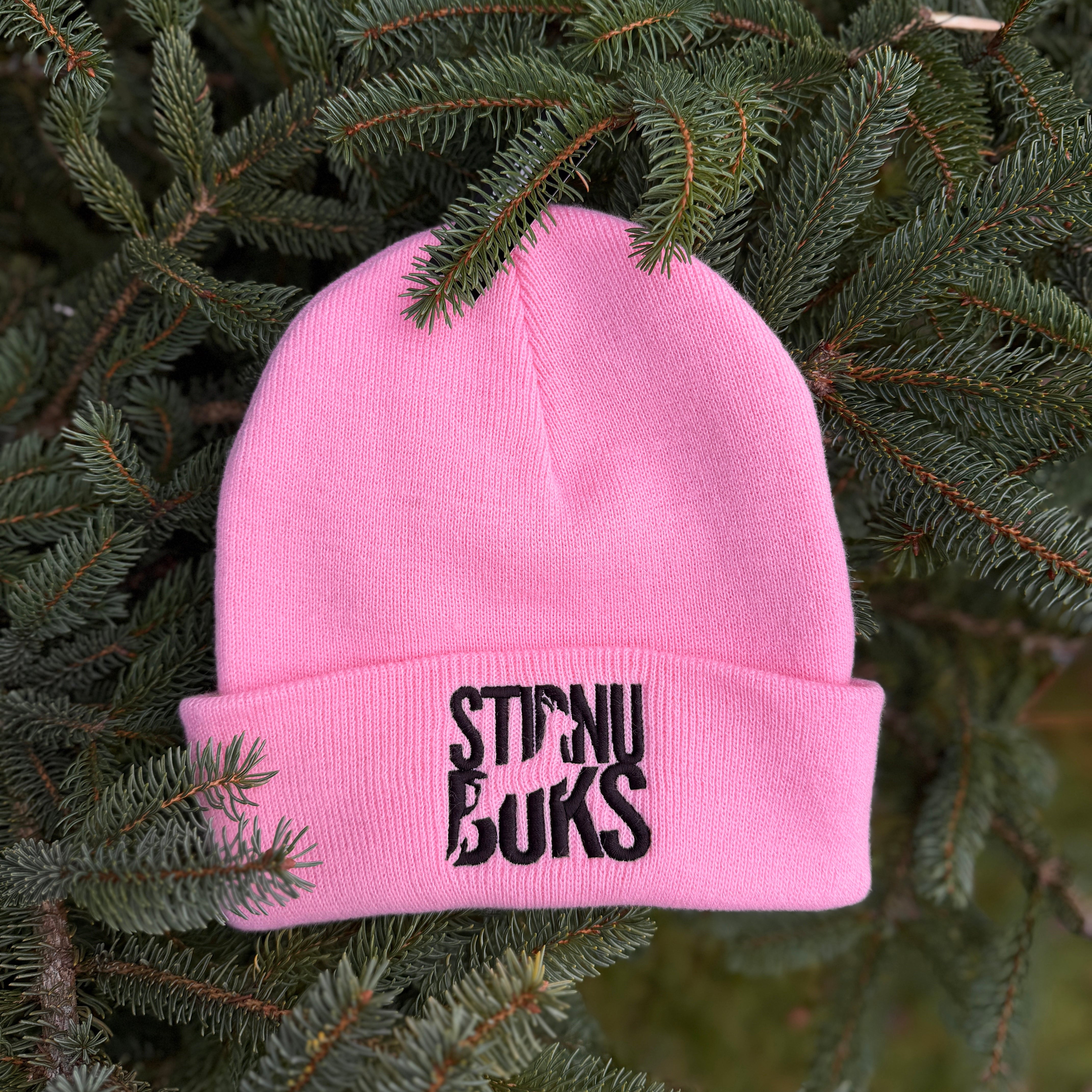 Pink beanie with 'STIRNU BUKS' text on a green leafy background